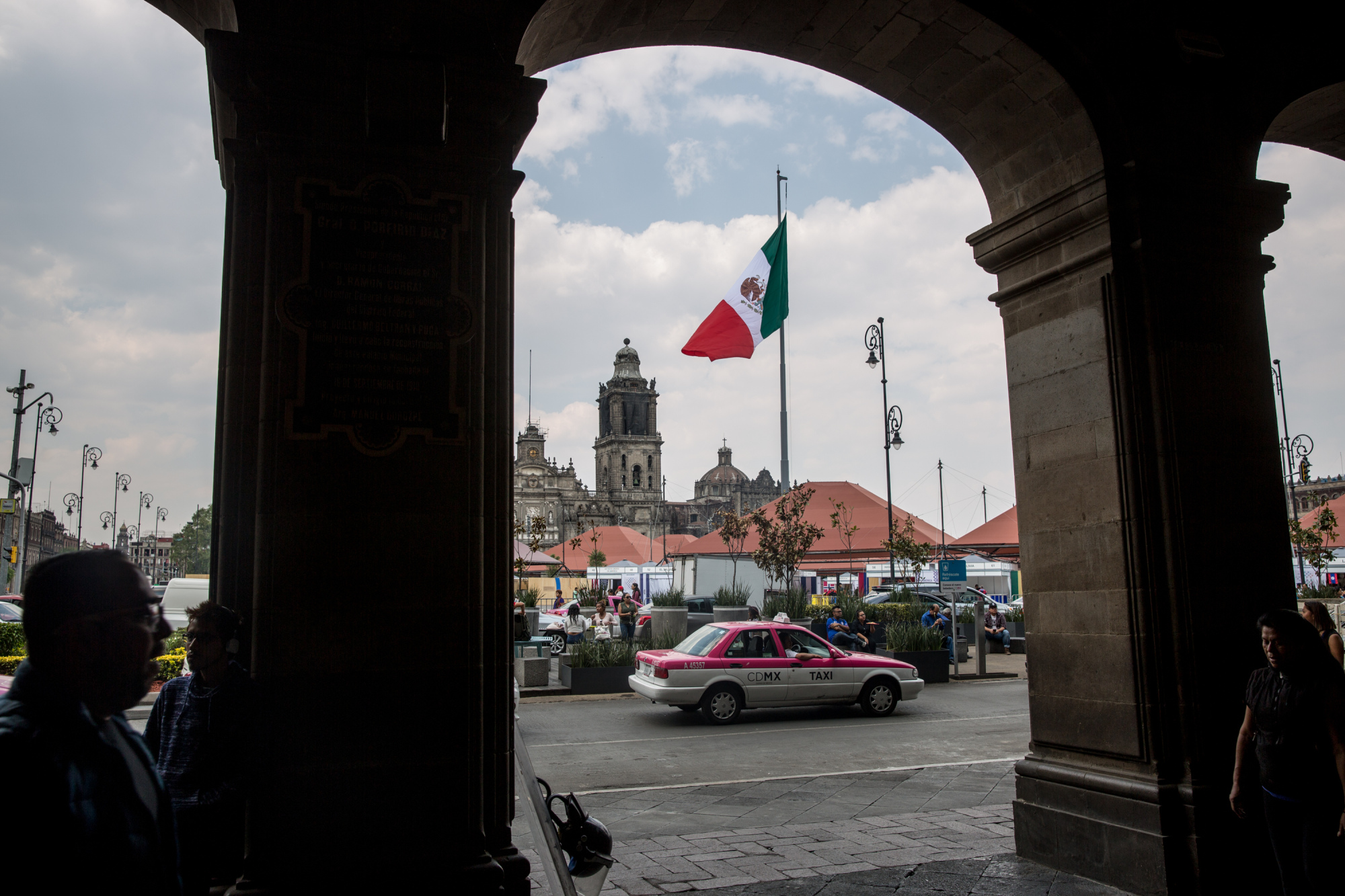 A taxi cab passes in front of the Mexican flag flying at the Plaza de la Constitucion (Zocalo) in Mexico City, Mexico, on Friday, April 13, 2018.