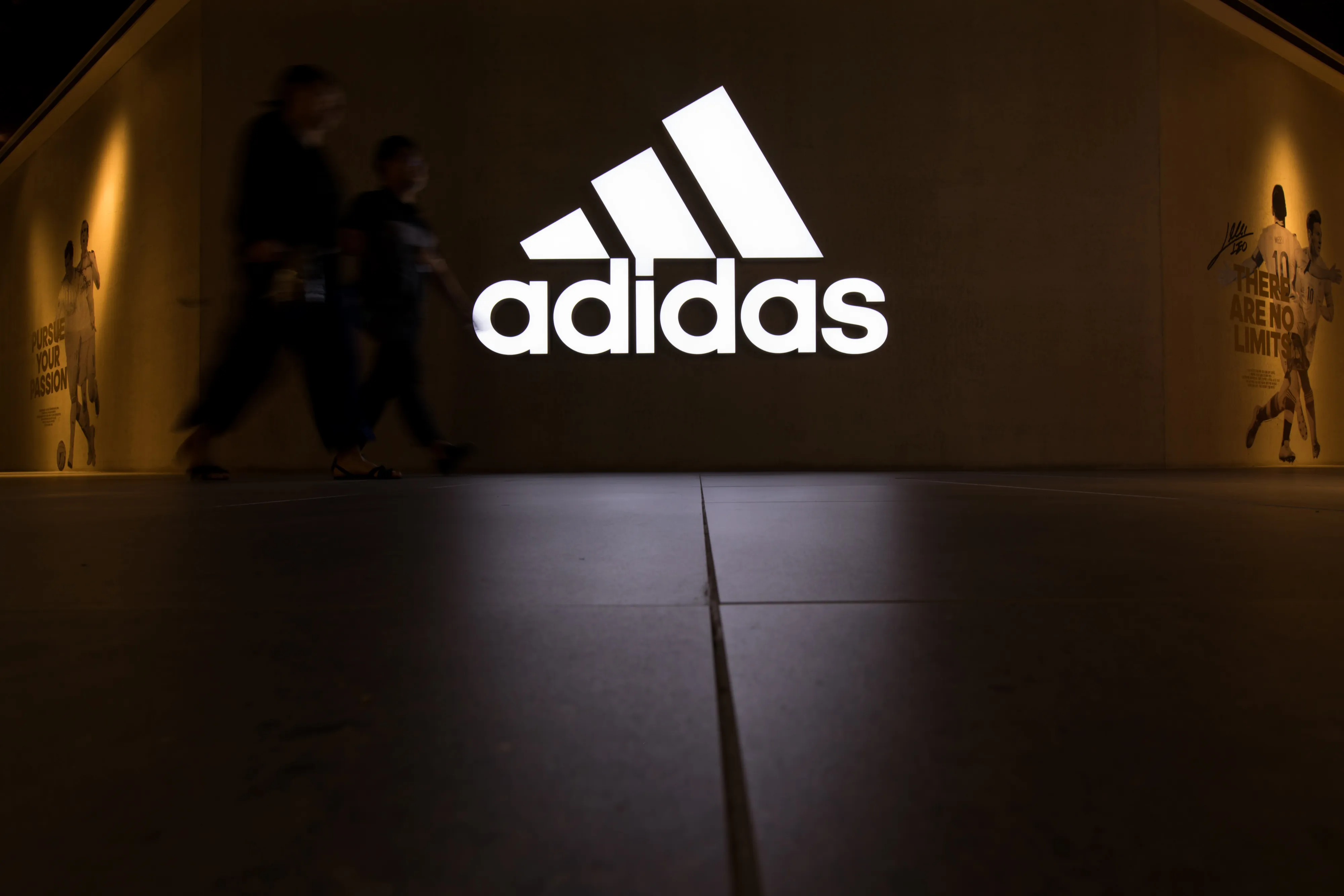 People walk past an illuminated Adidas sign.
