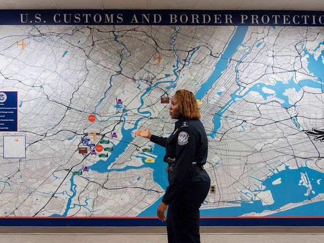 A female police officer standing and gesturing toward a large wall-size map of New York City and surrounding regions.