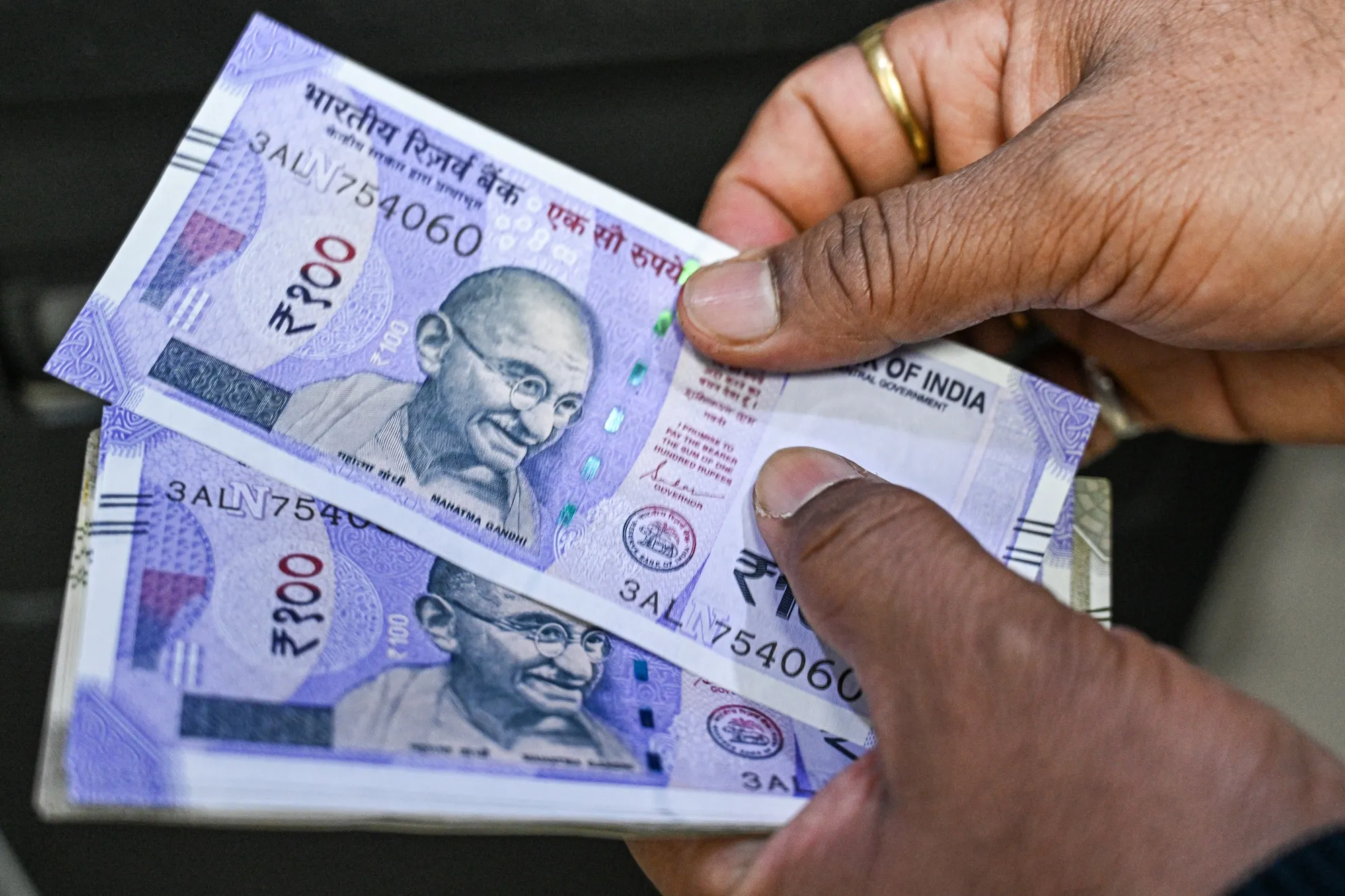 A customer counts 100 rupee banknotes after withdrawing them from an ATM in New Delhi