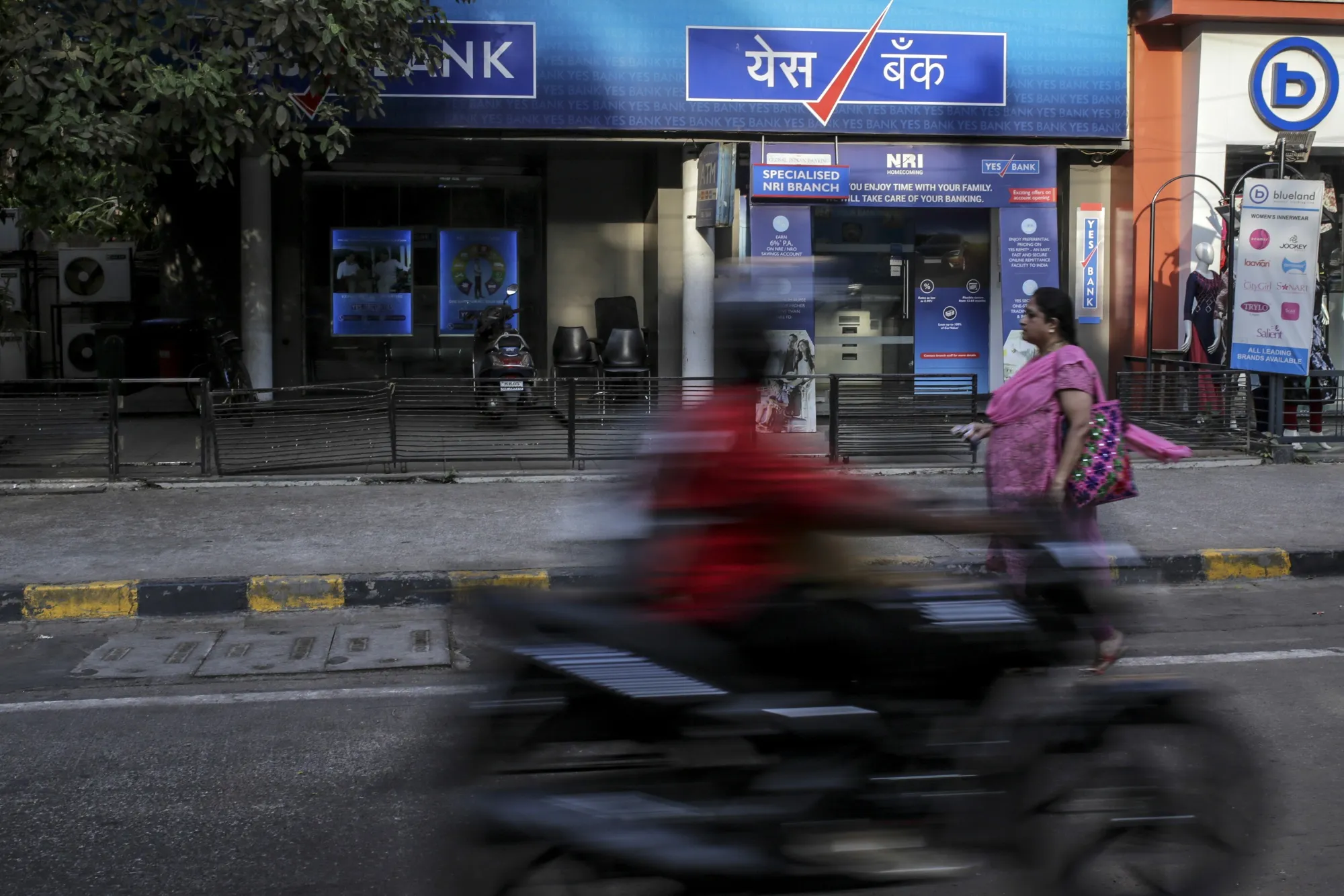 A pedestrian and motorcyclist pass a Yes Bank Ltd. branch in Mumbai, India.