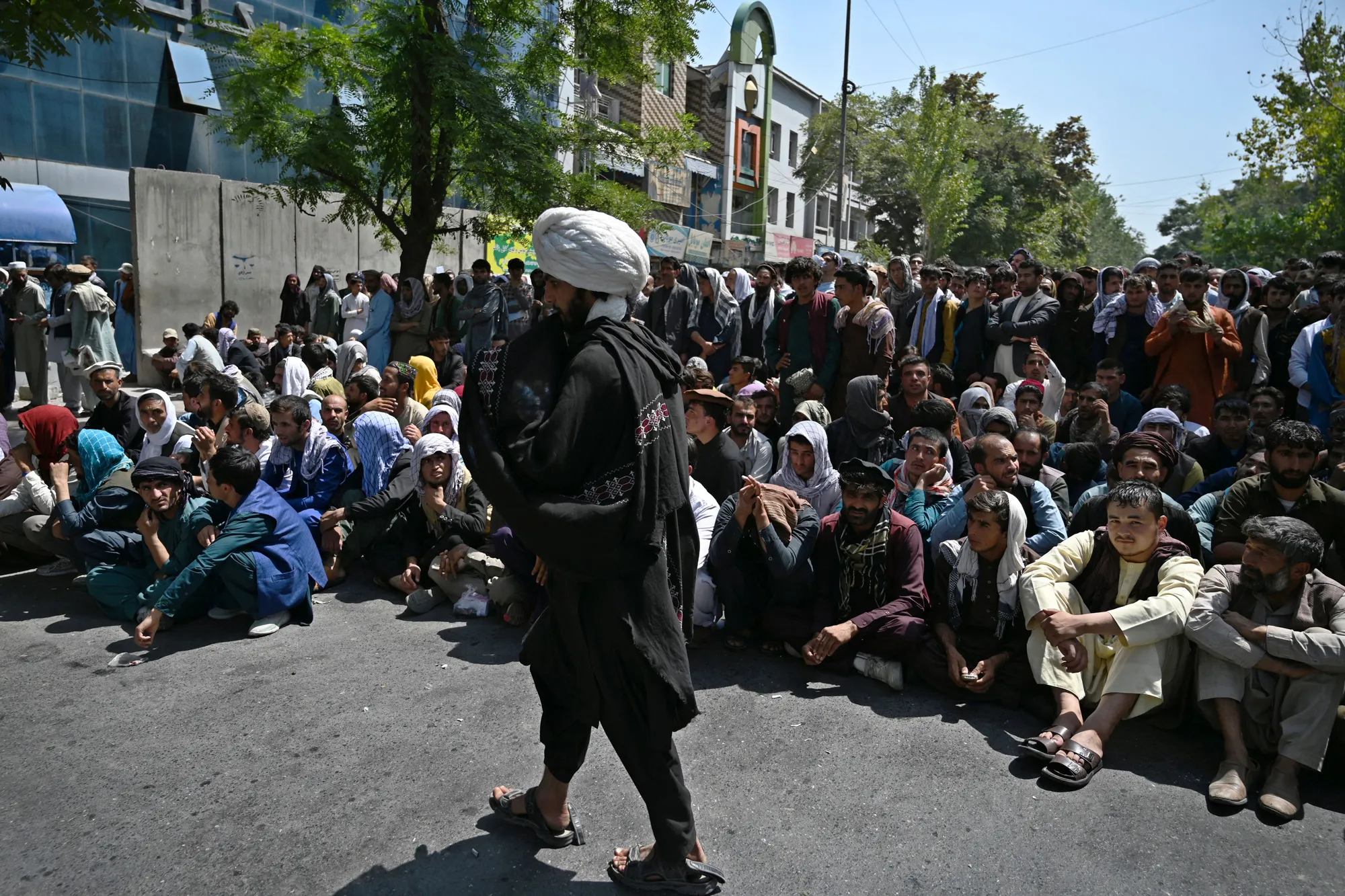 People sit and wait outside a bank to withdraw money&nbsp;in Kabul, in September.