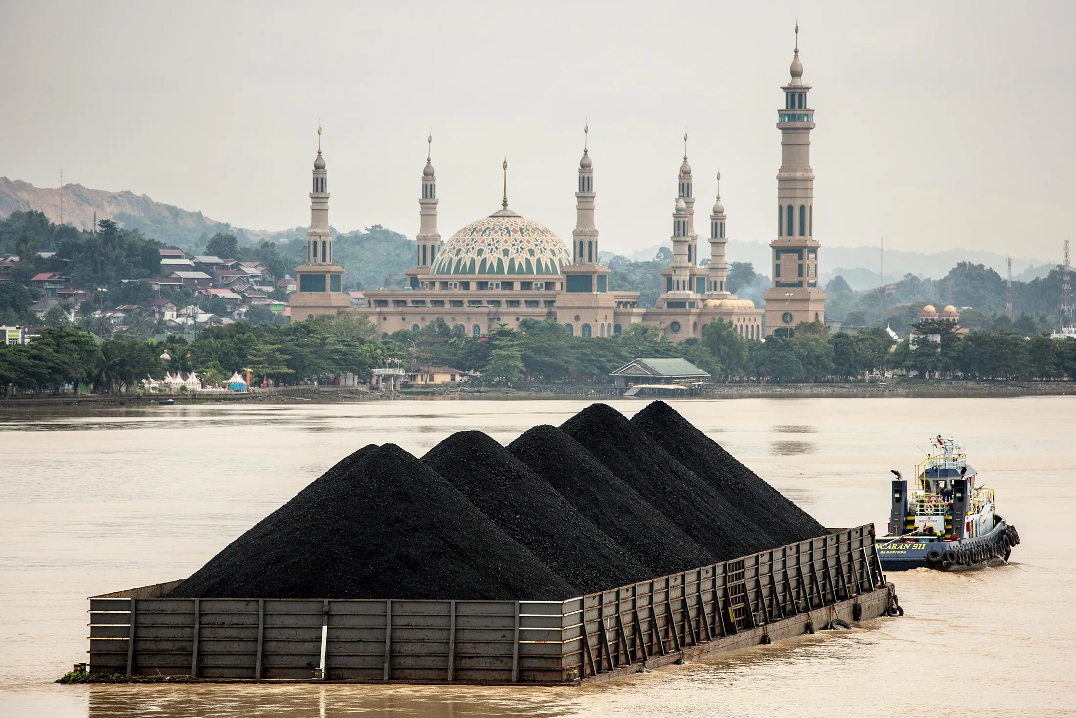 A tug pulls a coal barge past the Islamic centre on August 26, 2016 in Samarinda, Kalimantan, Indonesia.
