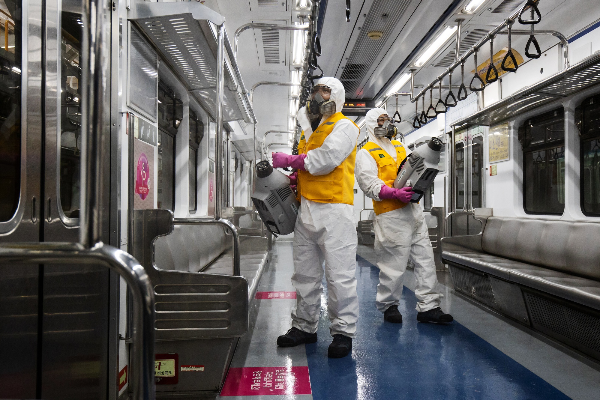 Workers wearing protective suits and masks spray disinfectant inside a Seoul Metro subway train.