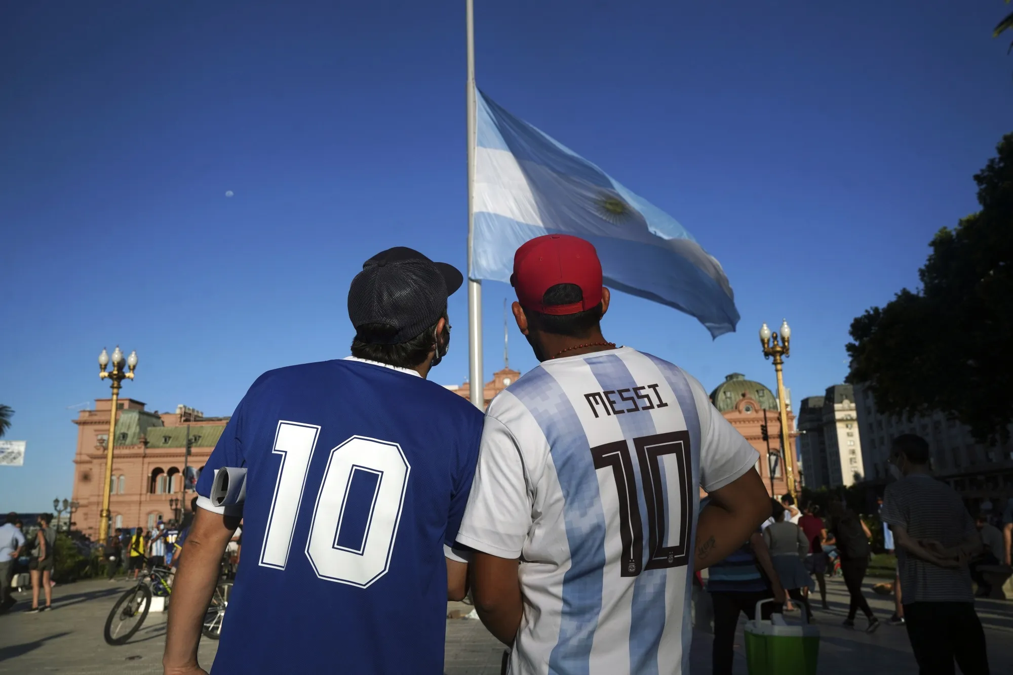 People stand in front of the Argentina flag in half-mast during a tribute to the late Argentine football star Diego Maradona, outside the Casa Rosada presidential palace in Buenos Aires, Argentina, on Thursday, Nov. 26, 2020.&nbsp;