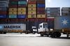 Trucks carry shipping containers next to a cargo ship docked in the APM Terminals yard at the Port of Mobile in Mobile, Alabama.