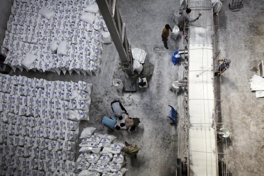 Workers, right, break and mix sugar crystals on a conveyor as others pack bags of candy sugar at a manufacturing plant in Simbhaoli, Uttar Pradesh.