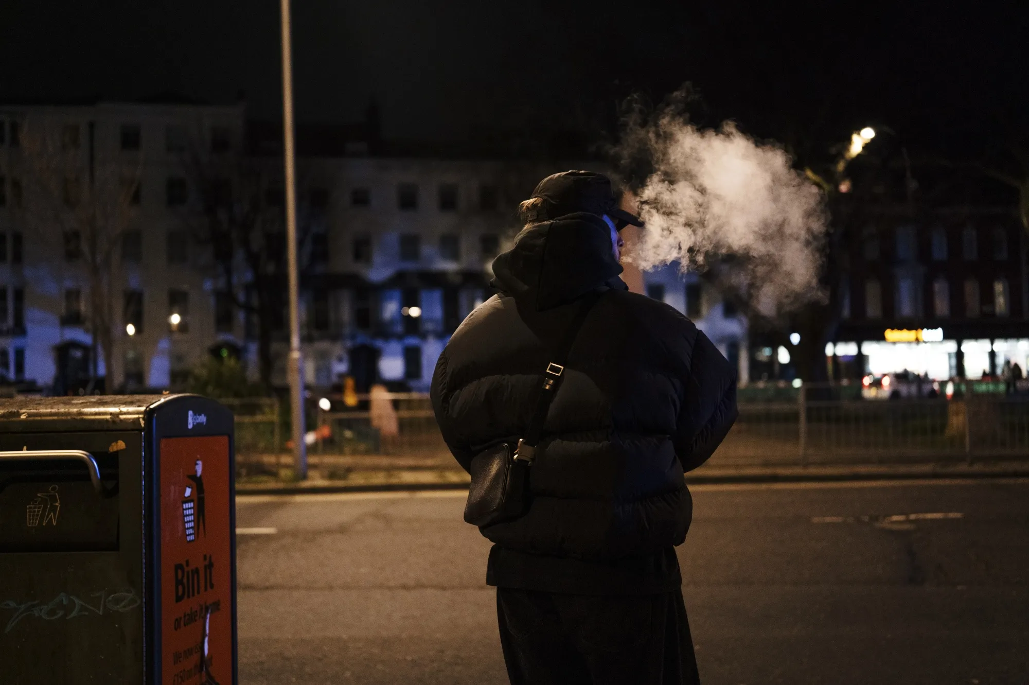 A man vapes while waiting for the bus.