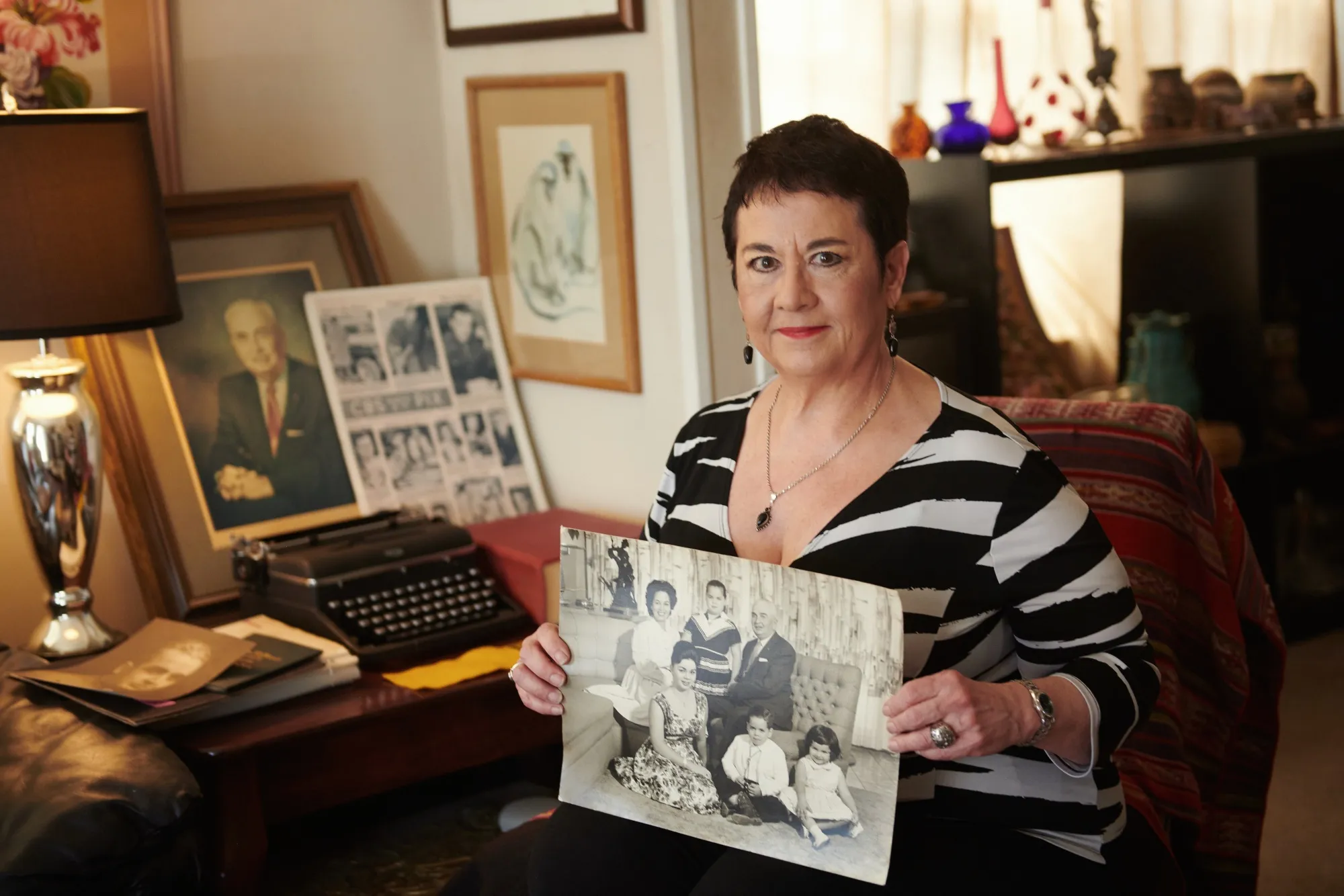 Carolyn Chester holds a childhood photograph oin the bottom right corner, alongside her parents, Edmund and Enna “Nena” Chester, and her siblings, at their home in Florida.