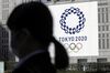 A pedestrian walks past a banner featuring the emblem for the Tokyo 2020 Olympic Games in Tokyo, Japan.