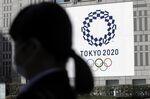 A pedestrian walks past a banner featuring the emblem for the Tokyo 2020 Olympic Games in Tokyo, Japan.