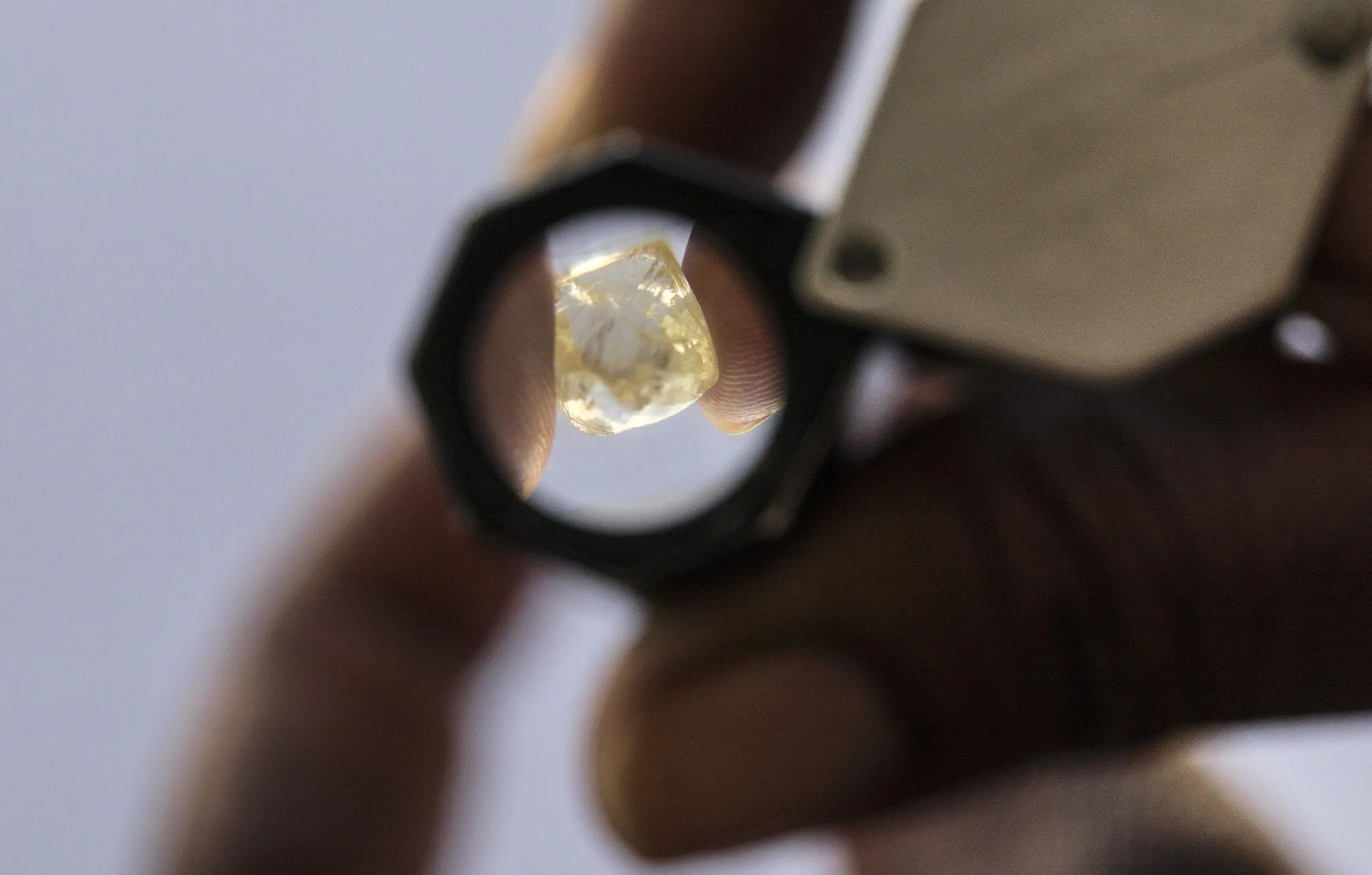 A large rough diamond is viewed through a loup.