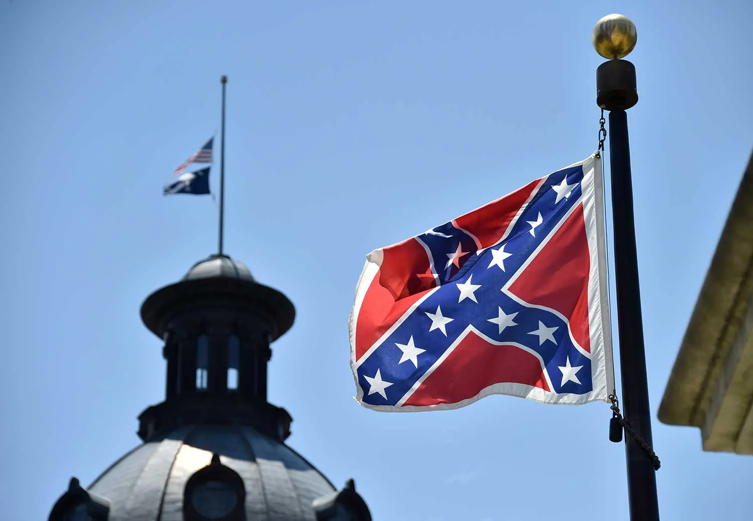 The South Carolina and US flags are seen flying at half-staff behind the Confederate flag erected in front of the State Congress building in Columbia, South Carolina on June 19, 2015. Police captured the white suspect in a gun massacre at one of the oldest black churches in Charleston in the United States, the latest deadly assault to feed simmering racial tensions. Police detained 21-year-old Dylann Roof, shown wearing the flags of defunct white supremacist regimes in pictures taken from social media, after nine churchgoers were shot dead during bible study on Wednesday.
