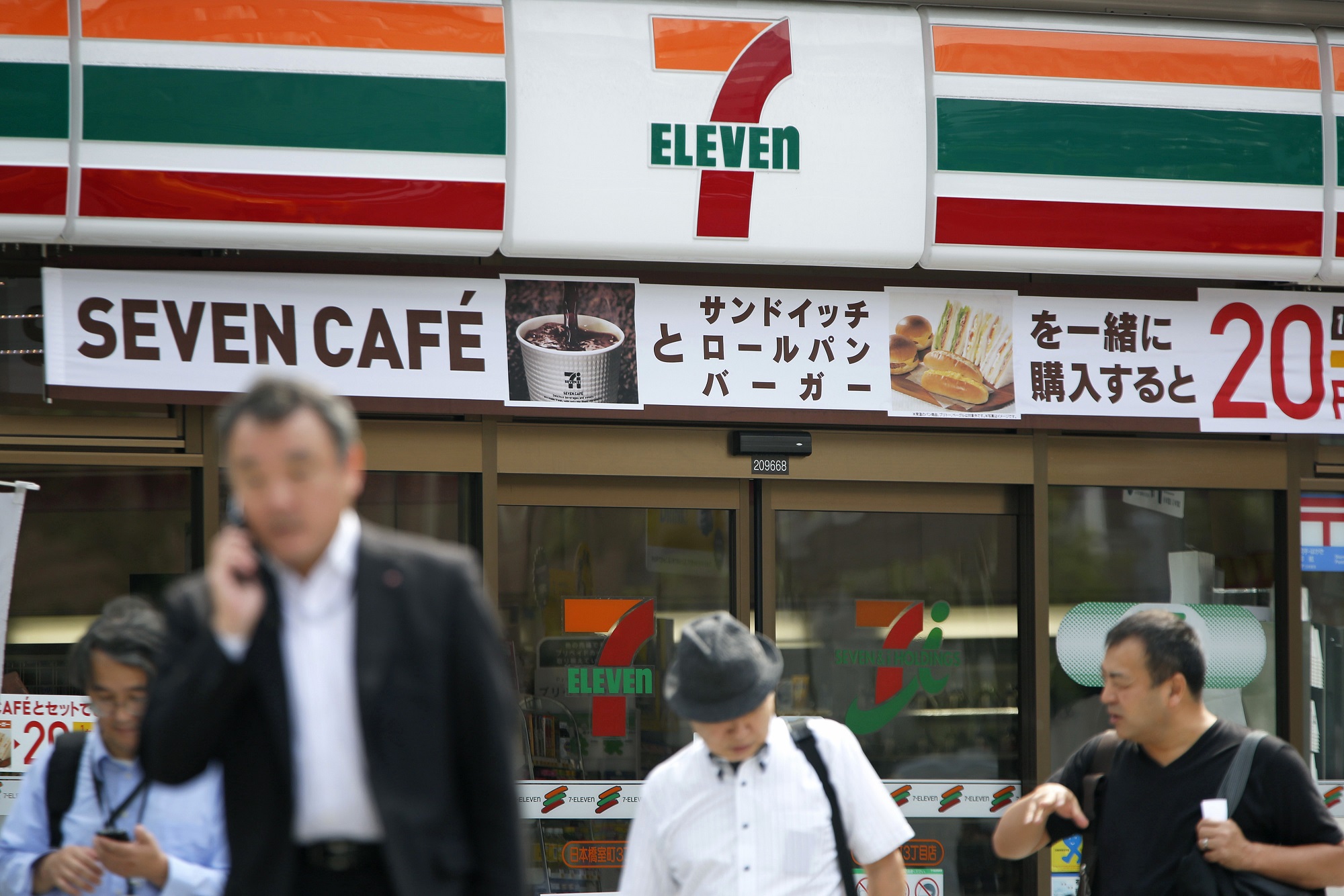 Pedestrians walk in front of a 7-Eleven convenience store in Tokyo, Japan.
