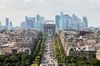 The Arc De Triomphe stands while automobiles travel on the Avenue des Champs-Elysees as skyscrapers sit on the city skyline in the La Defense business district in Paris, France.