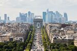 The Arc De Triomphe stands while automobiles travel on the Avenue des Champs-Elysees as skyscrapers sit on the city skyline in the La Defense business district in Paris, France.