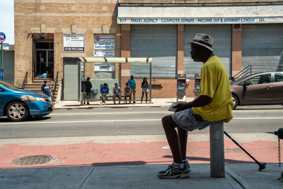A man sits in the shade as people wait at a bus stop in the Bronx borough of New York City. Some cities are installing more shelters to provide better refuge from extreme heat.