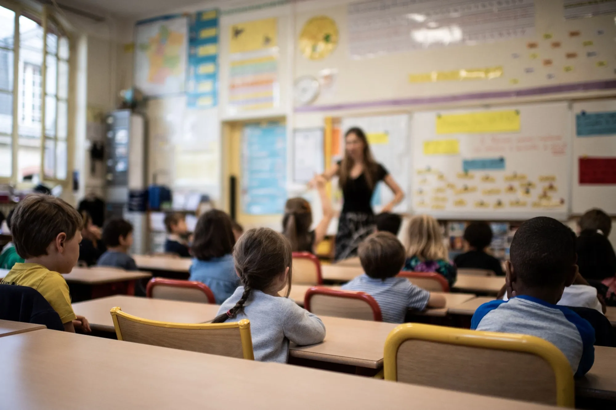 Children listen to their teacher as they sit in a classroom.