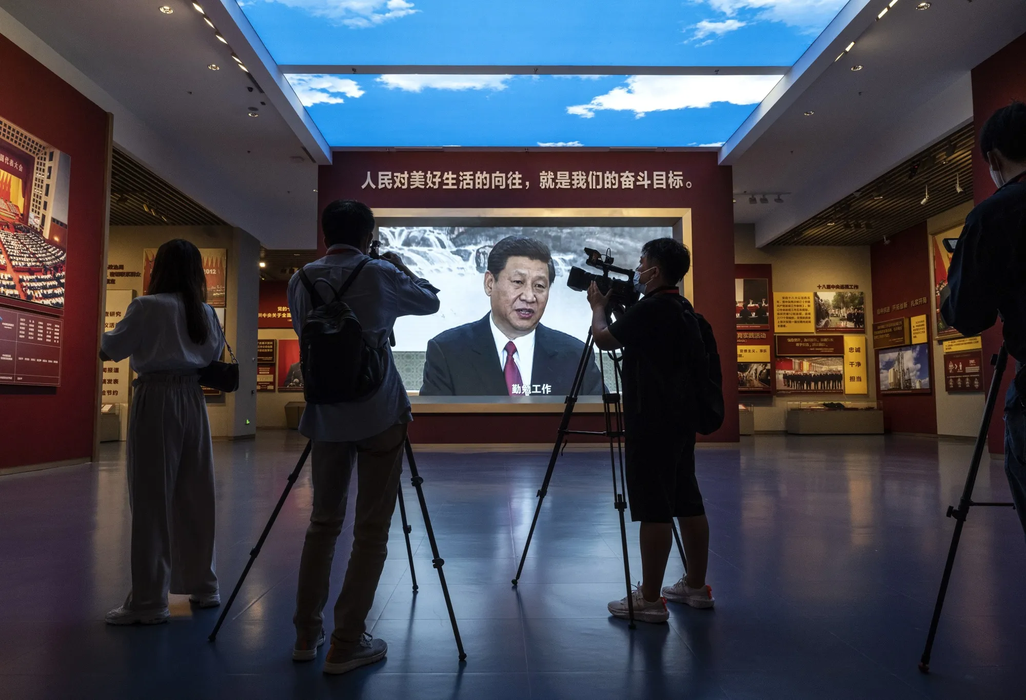 Journalists and others film next to a large screen showing President Xi Jinping.