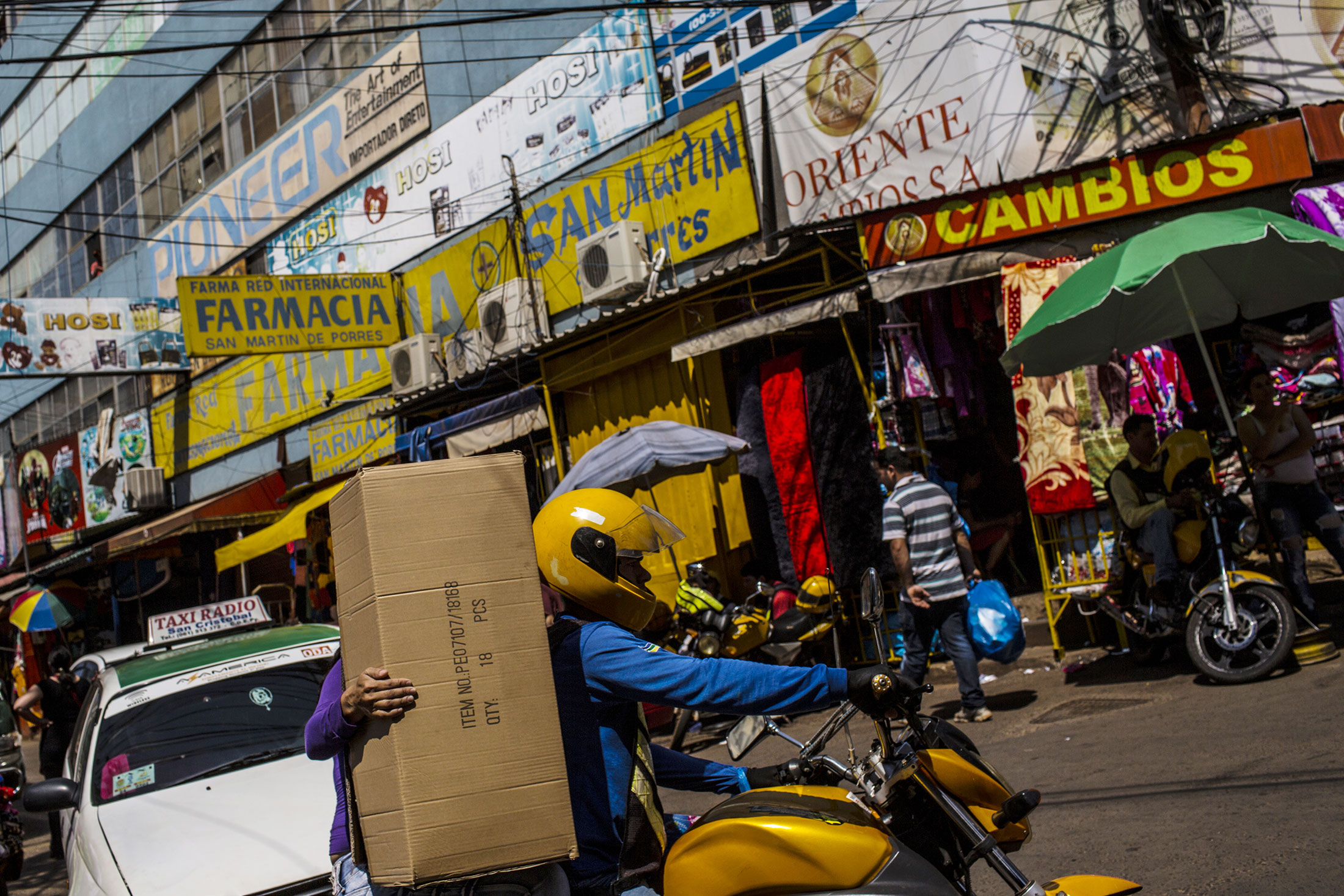 A taxi and a motorcycle drive on a busy commercial street in Ciudad del Este, Paraguay,
