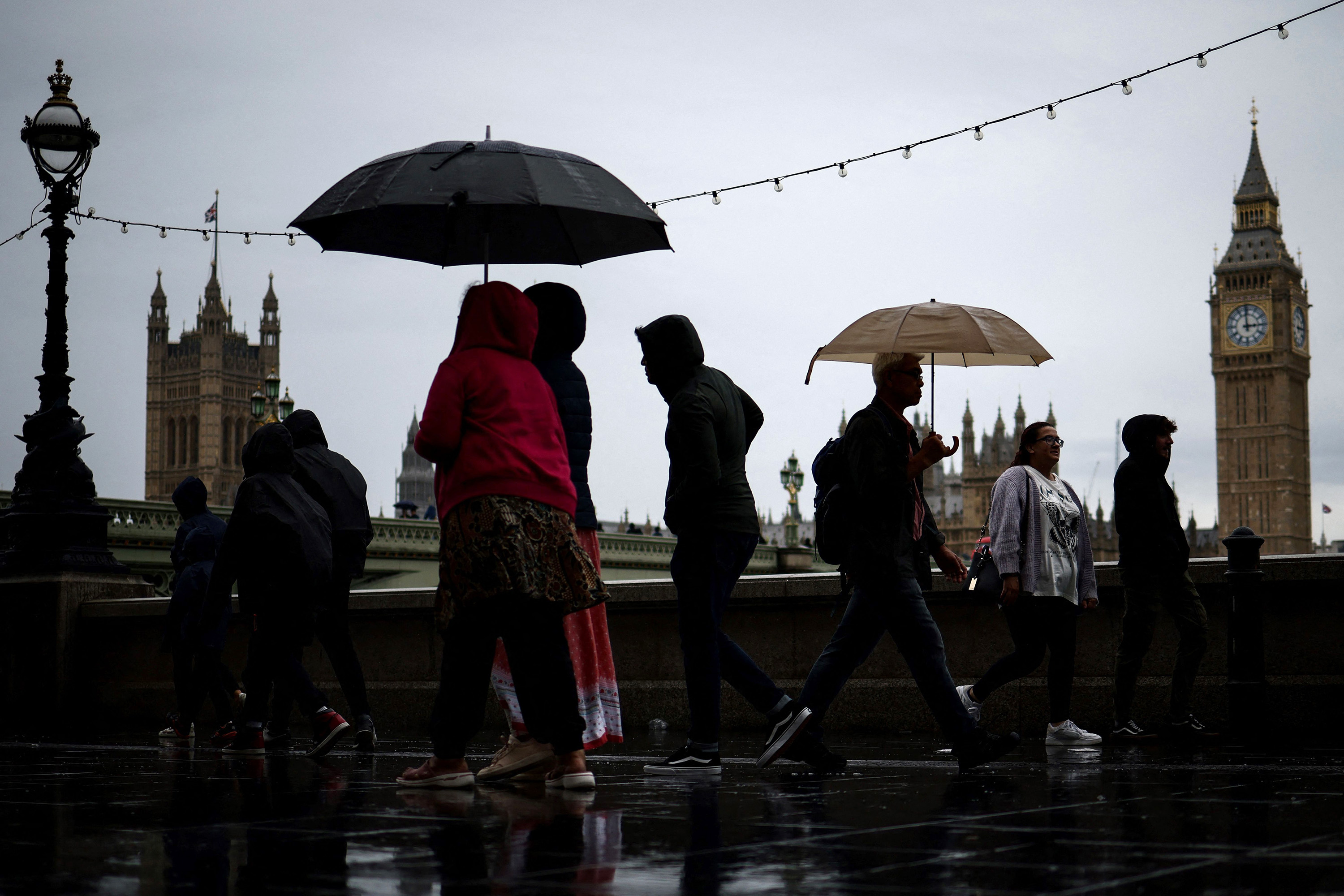 People sheltering from the rain beneath umbrellas walk past a