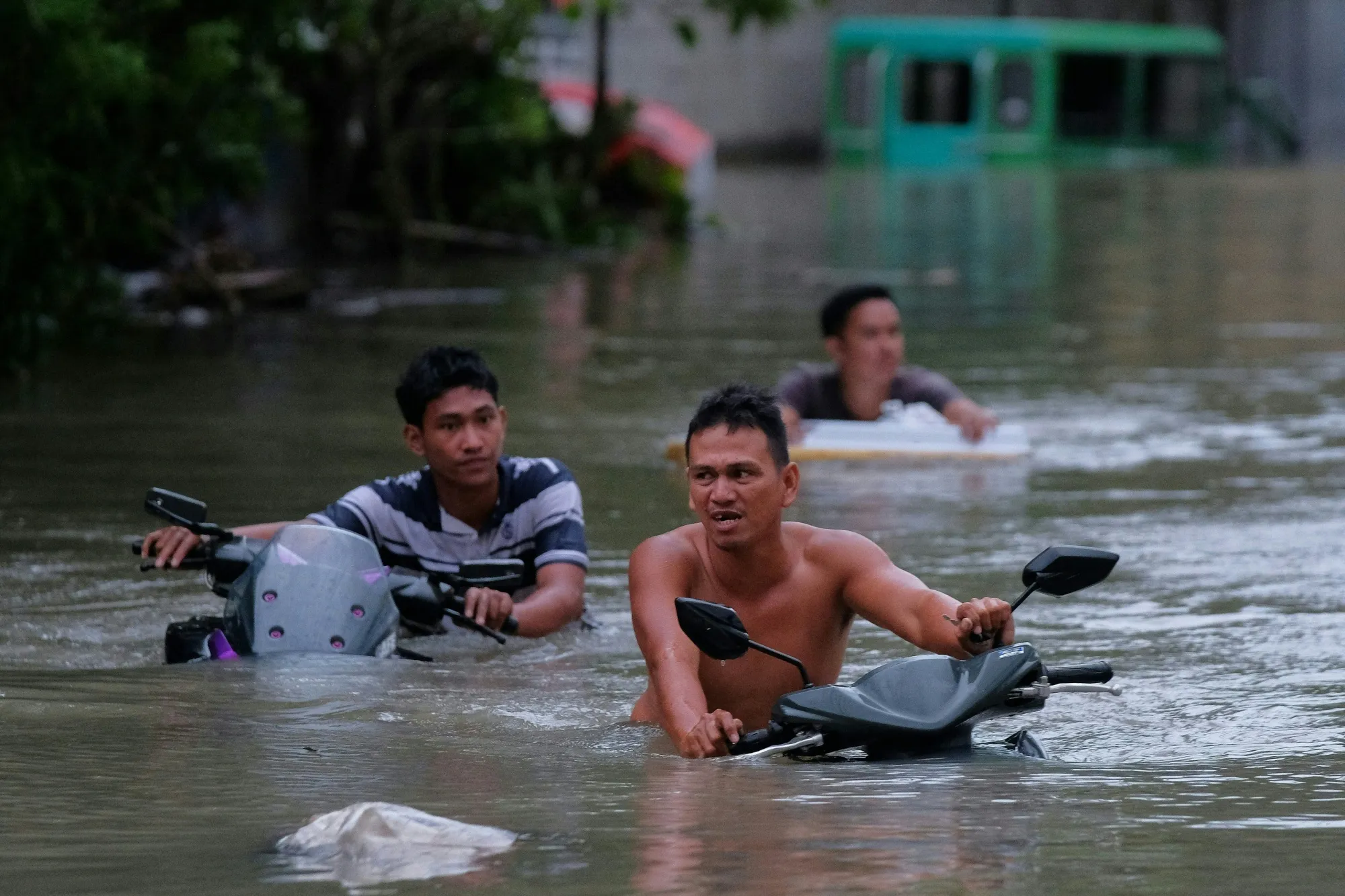 Residents push their motorcycles through a flooded street caused by heavy rains brought about by Tropical Storm Trami in Naga City, Camarines Sur province on Oct. 24.