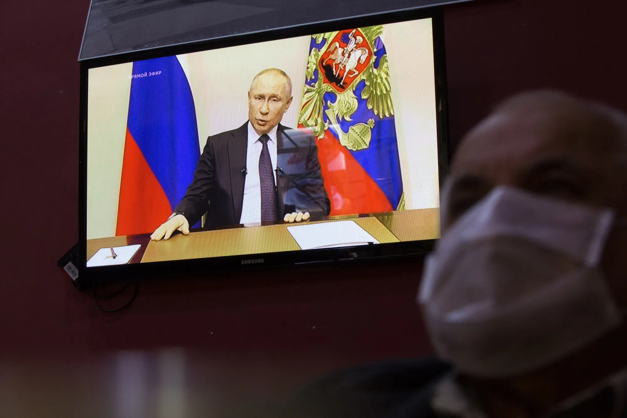 A customers wears a protective face mask inside a cafe as a television screen displays Vladimir Putin.