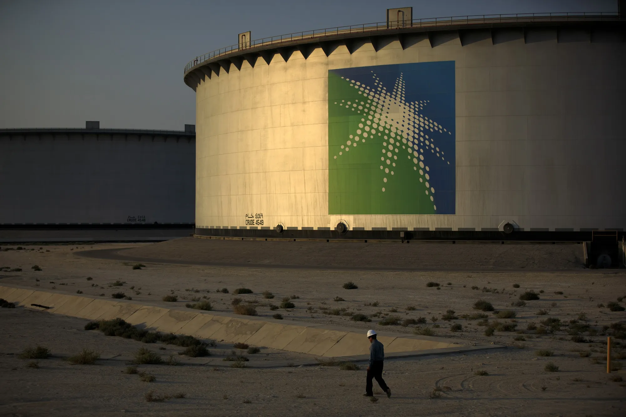 An employee walks past crude oil storage tanks at the Juaymah Tank Farm in Saudi Aramco's Ras Tanura oil refinery and oil terminal in Ras Tanura, Saudi Arabia.