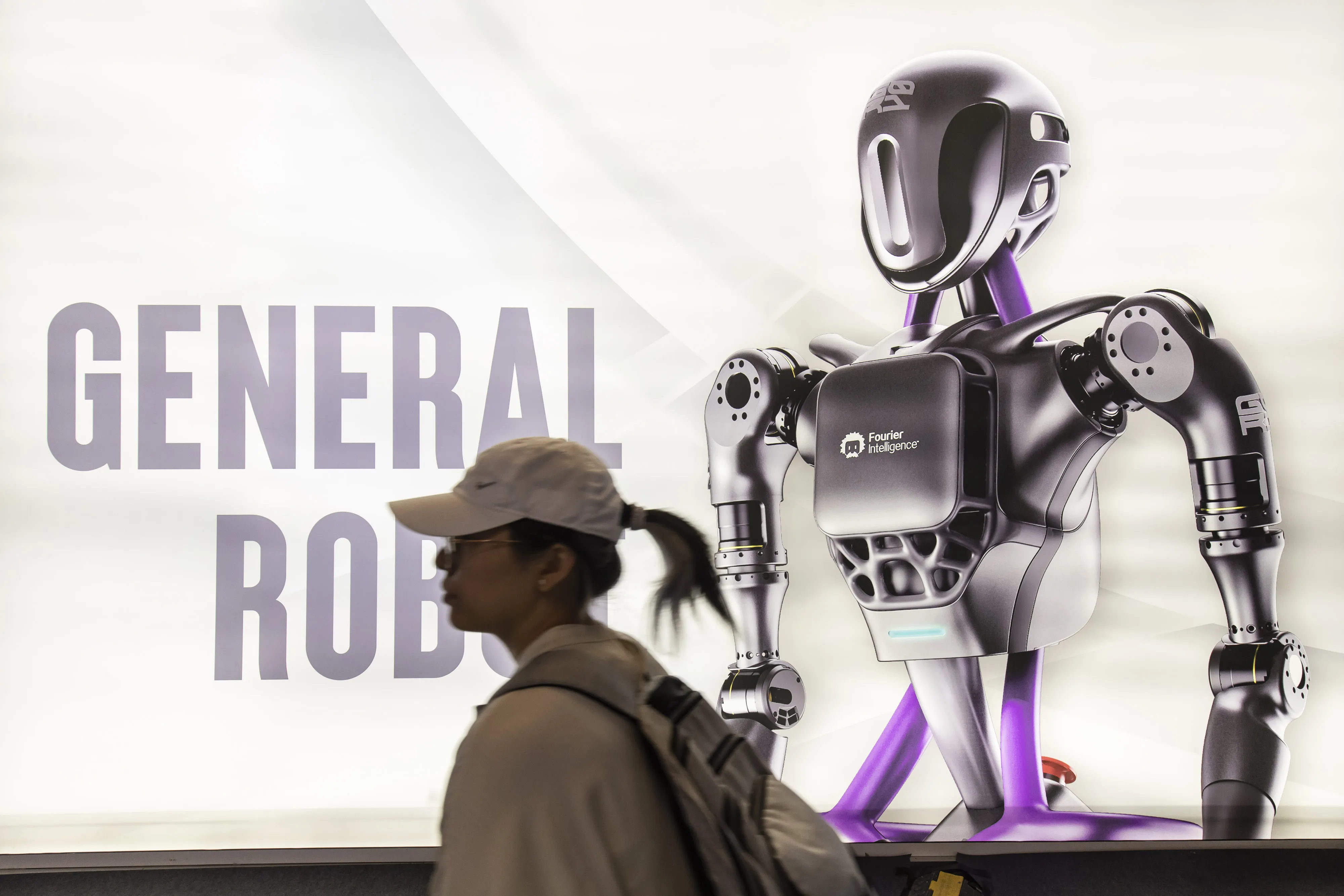 An attendee at the World AI Conference&nbsp;walks by a General Robot poster in Shanghai on Friday.