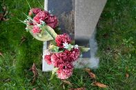 Bunch of old red artificial flowers seen in a brass vase by a grande gravestone.