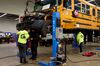 Three men are operating under a school bus that has been raised from the floor. Photographer: Gabby Jones/Bloomberg