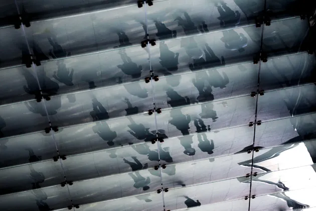 People are reflected in glass as they walk past Goldman Sachs headquarters in New York