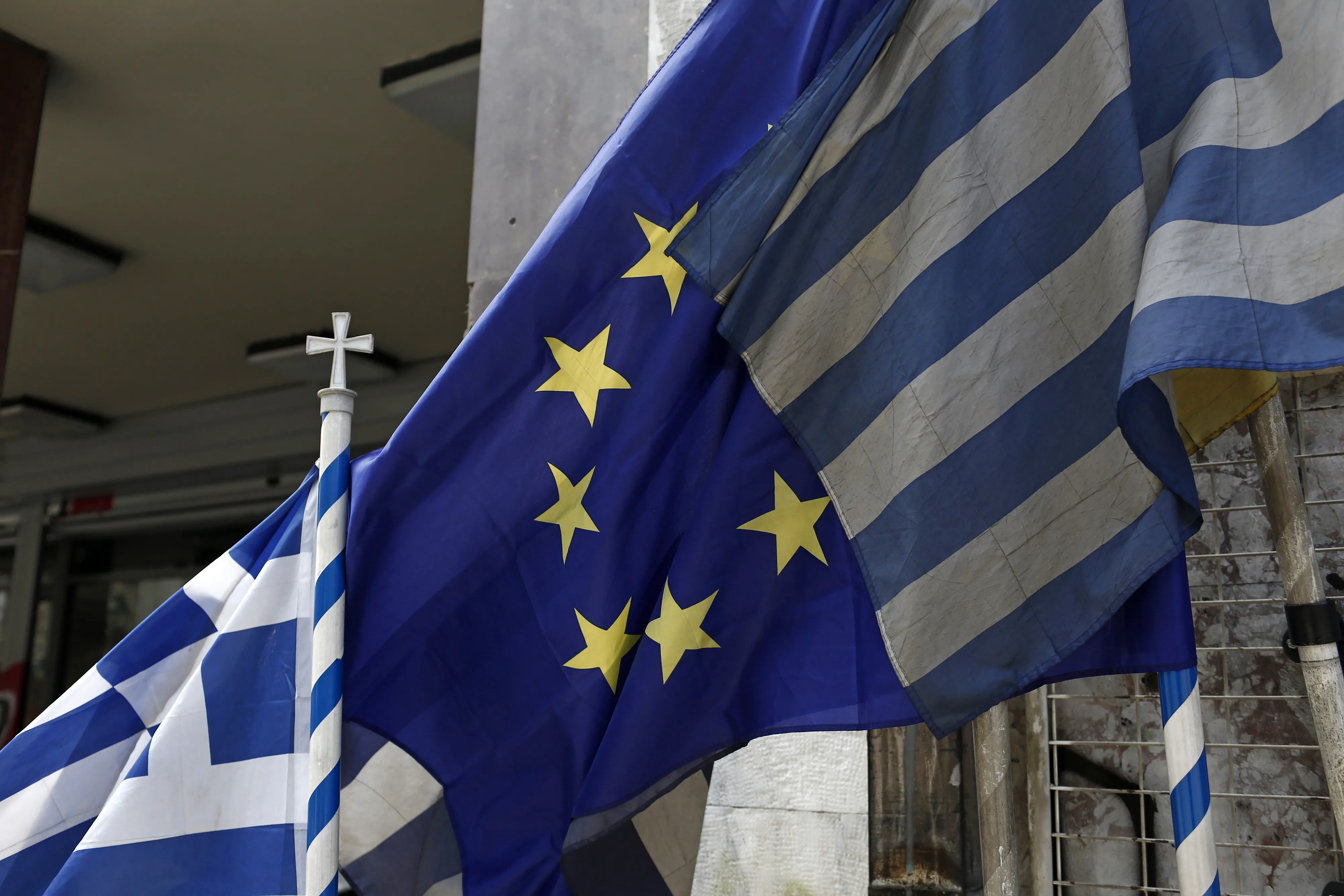 Greek national flags fly alongside a European Union flag outside a store in Athens, Greece.
