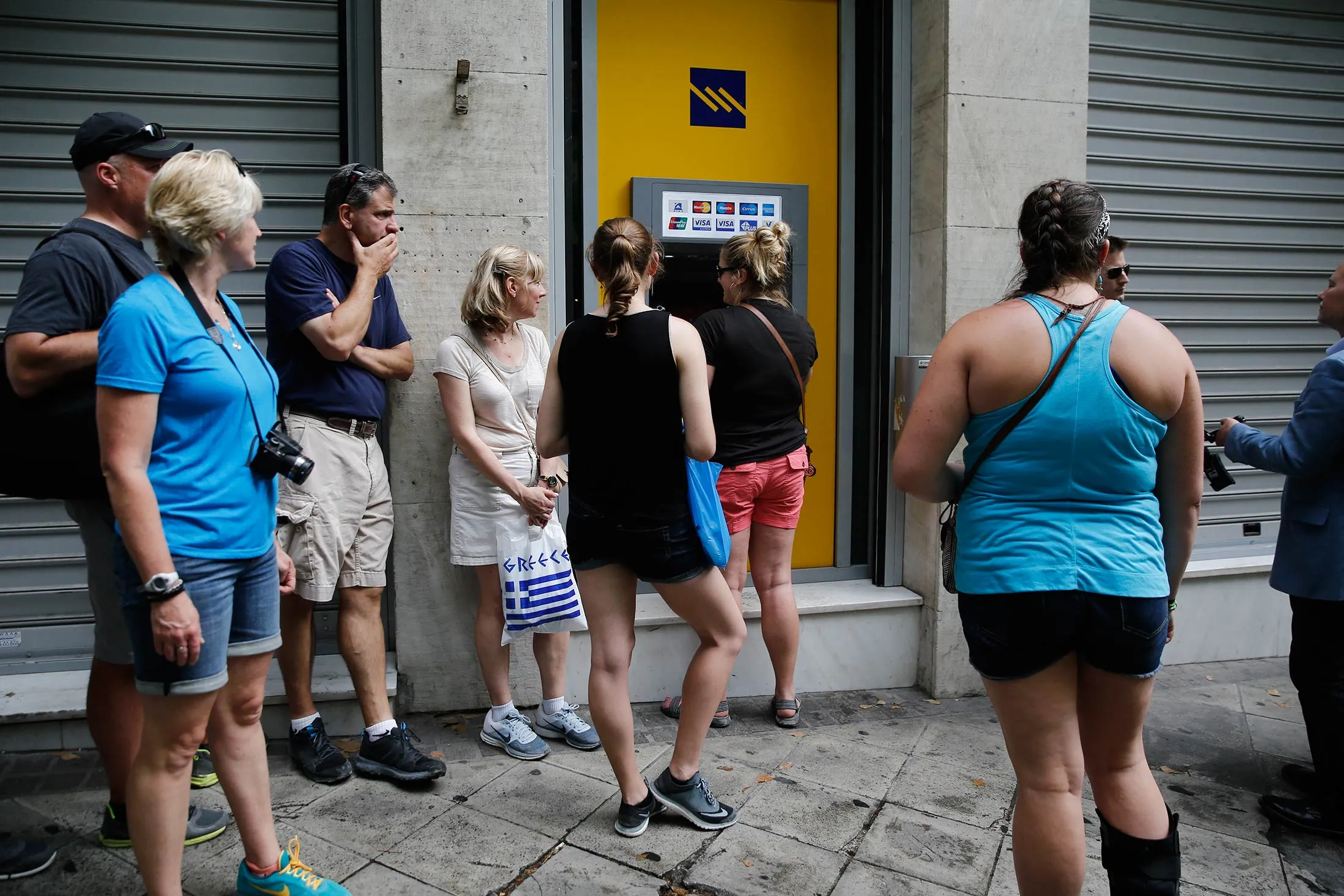 People wait in line at an automated teller machine (ATM) at a Piraeus Bank SA bank branch in Athens, Greece, on Monday, June 29, 2015.
