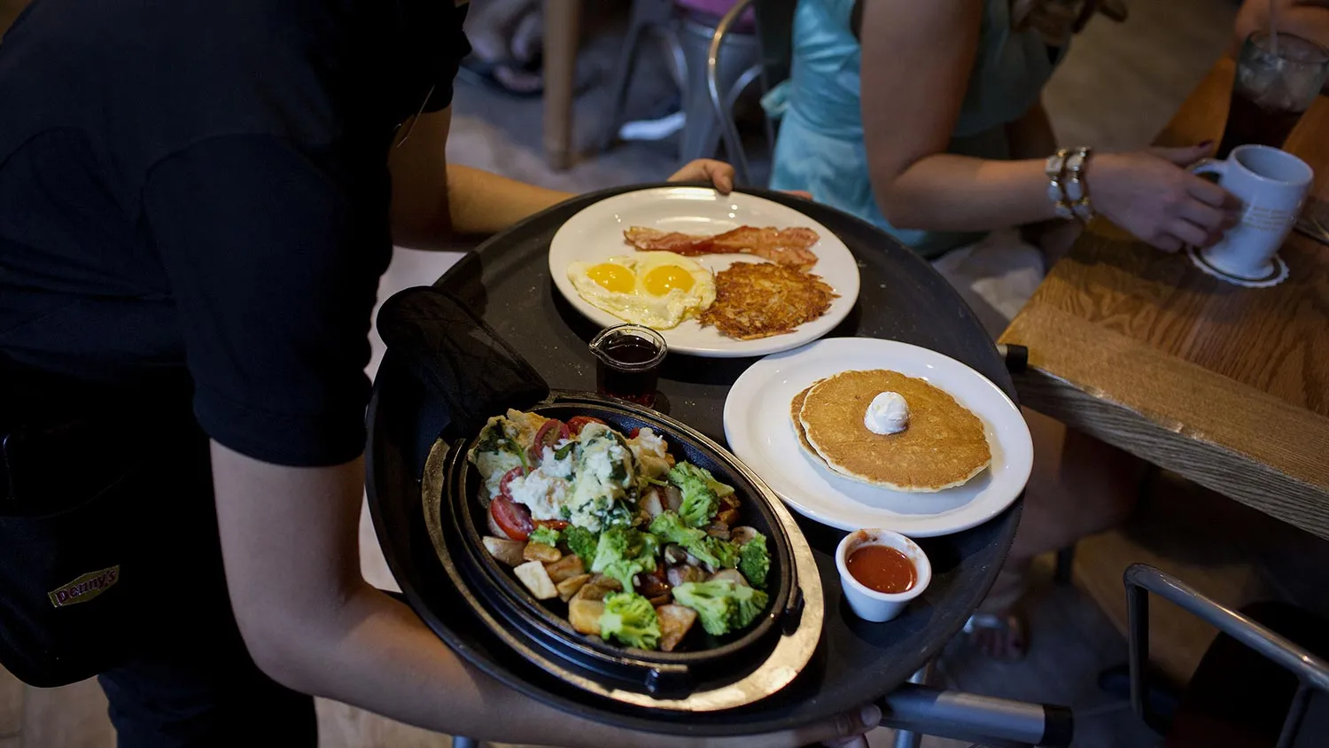 A waitress delivers a tray of food to customers at the Denny' s Corp. restaurant in New York, U.S., on Saturday, Sept. 6, 2014.
