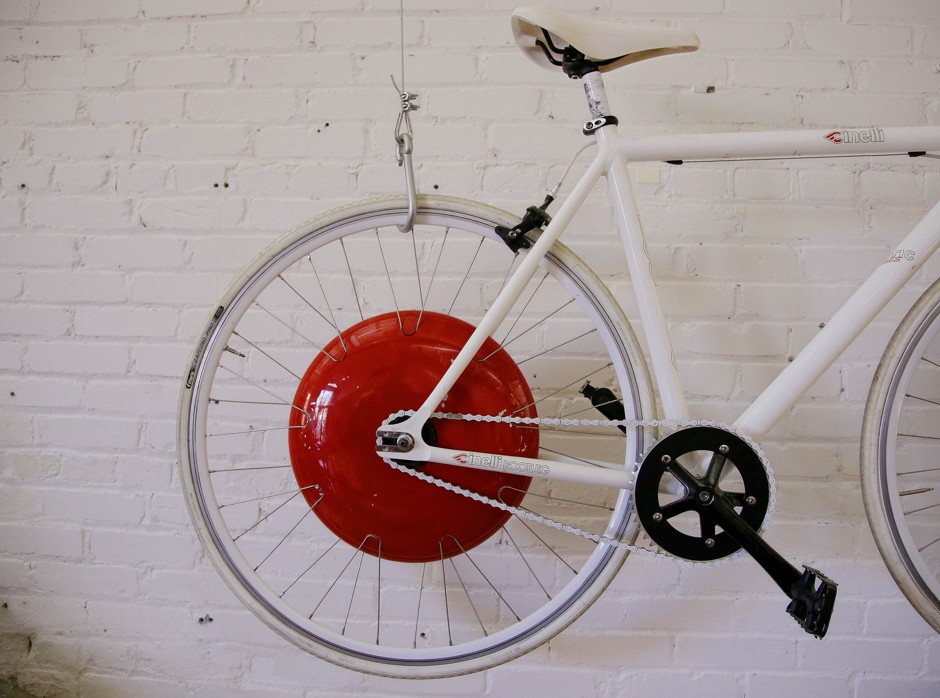 A bicycle fitted with a prototype of the Copenhagen Wheel, the red disk, human/electric hybrid bicycle engine, hangs on a wall at the Superpedestrian manufacturer in Cambridge, Massachusetts.