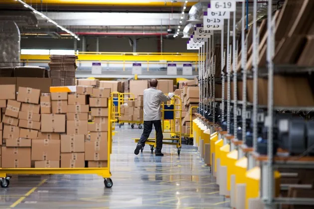 Shipping boxes sit on carts near product storage bays at an Amazon fulfillment center.
