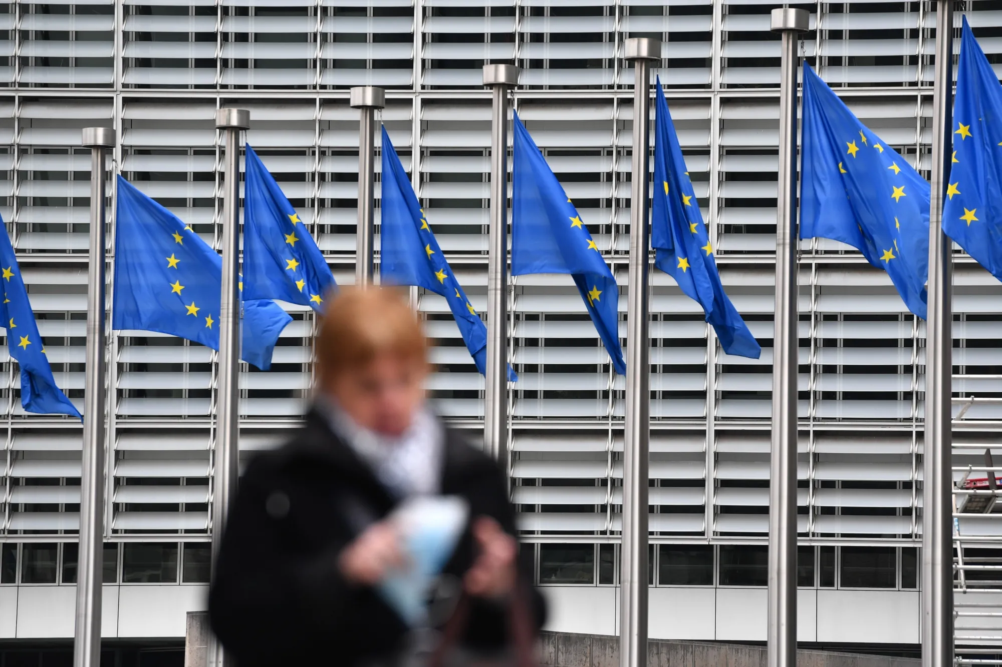 A pedestrian passes European Union (EU) flags flying outside the Berlaymont building in Brussels, Belgium.