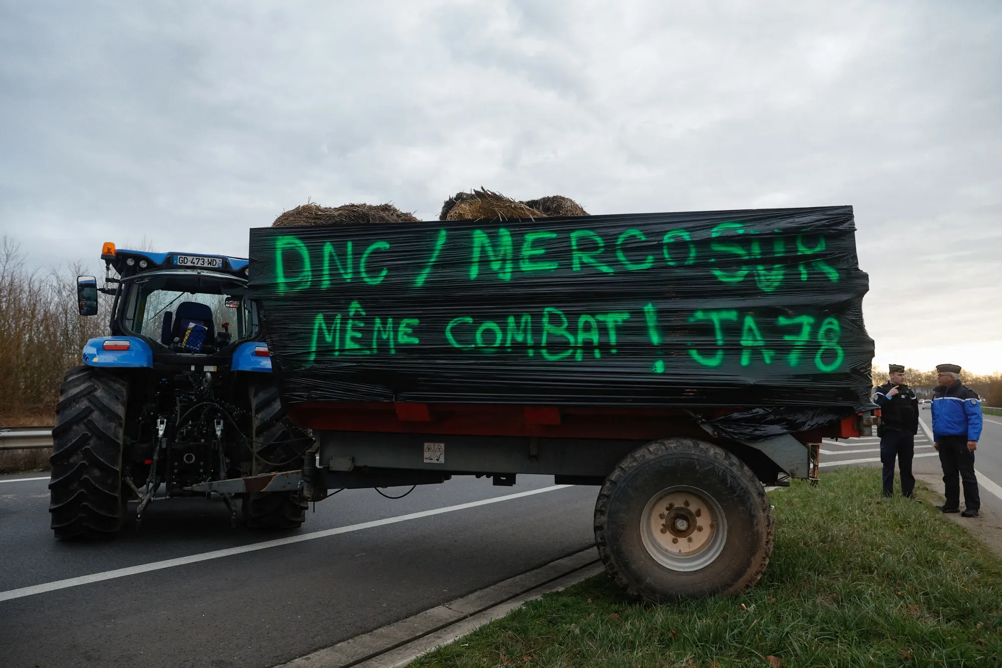 Farmers block a road with a sign on a tractor reading “DNC/Mercosur Same Battle” near Paris, on Dec. 16.