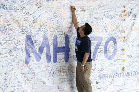 A man writes a message on a banner for missing Malaysian Airline System Bhd. Flight 370 at Kuala Lumpur International Airport (KLIA) in Sepang, on Friday, March 14, 2014