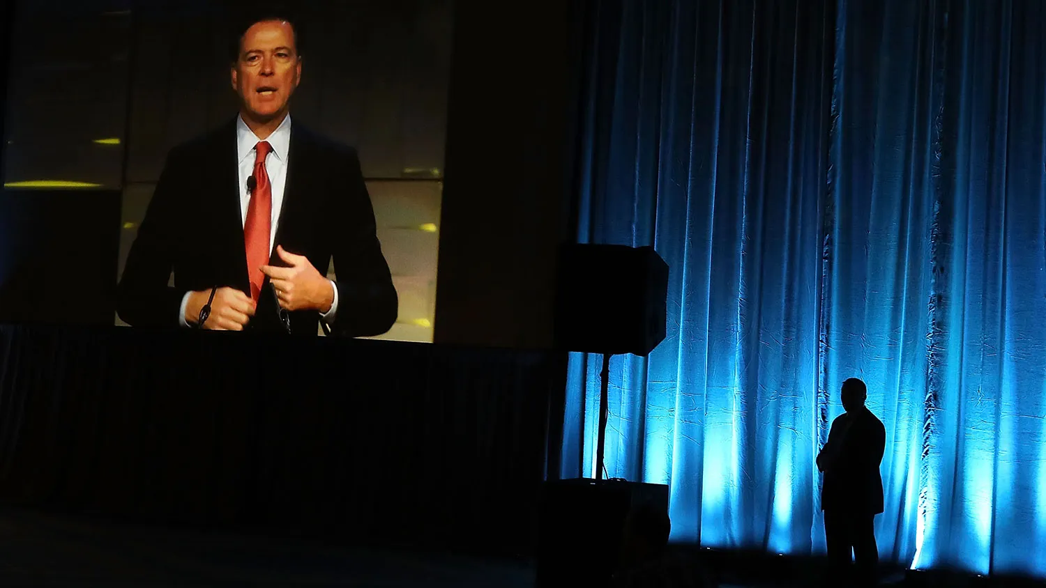 FBI Director James Comey is seen on a monitor speaking during a government symposium on cybersecurity on Aug. 30, 2016, in Washington.
