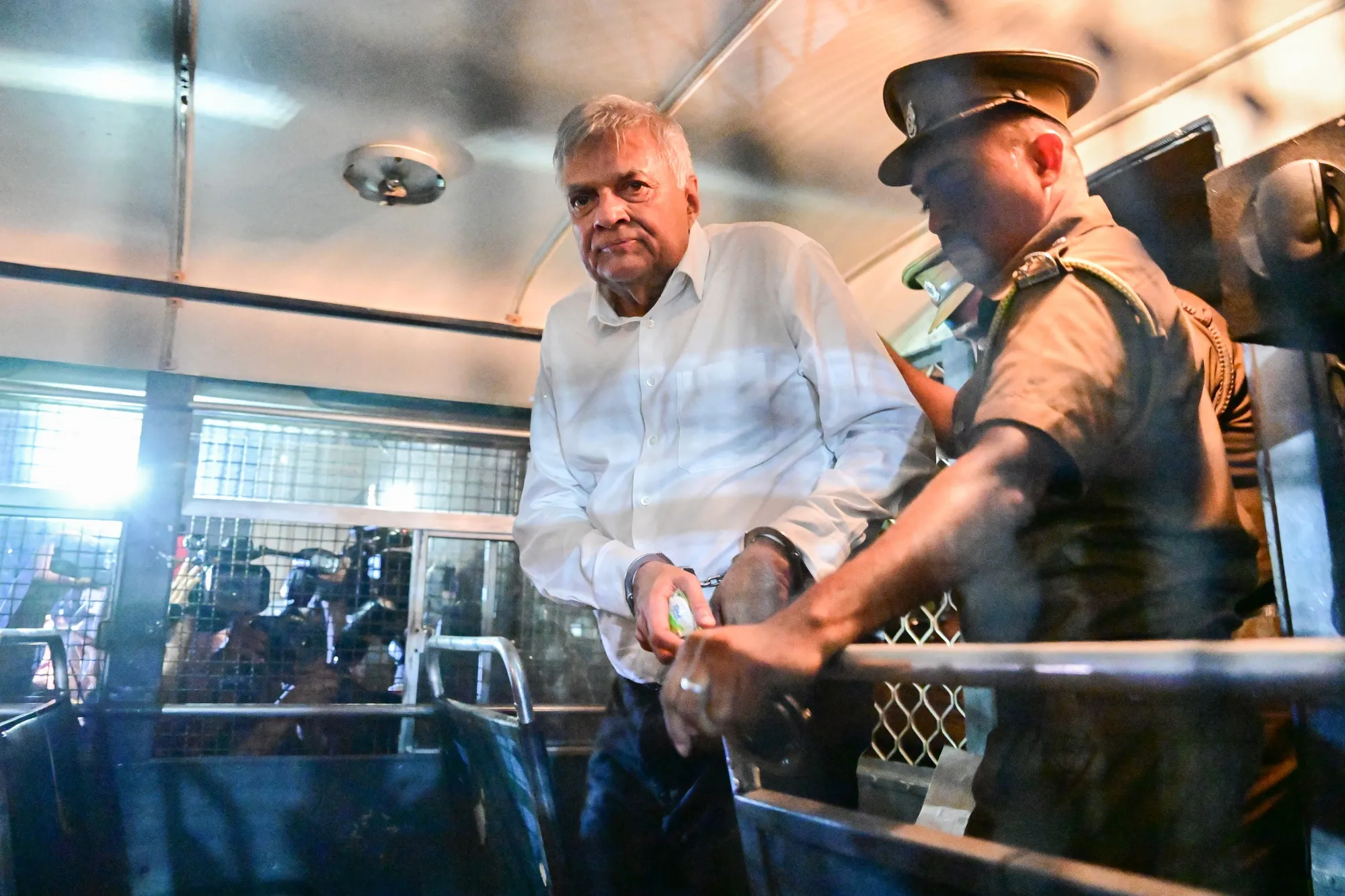 Sri Lanka's former President Ranil Wickremesinghe&nbsp;is escorted to his seat in a prison bus in Colombo, on Aug. 22.