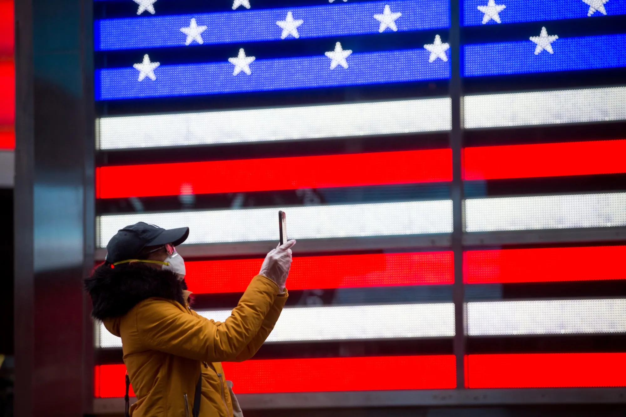 A pedestrian wearing a protective face mask takes a photograph in Times Square.
