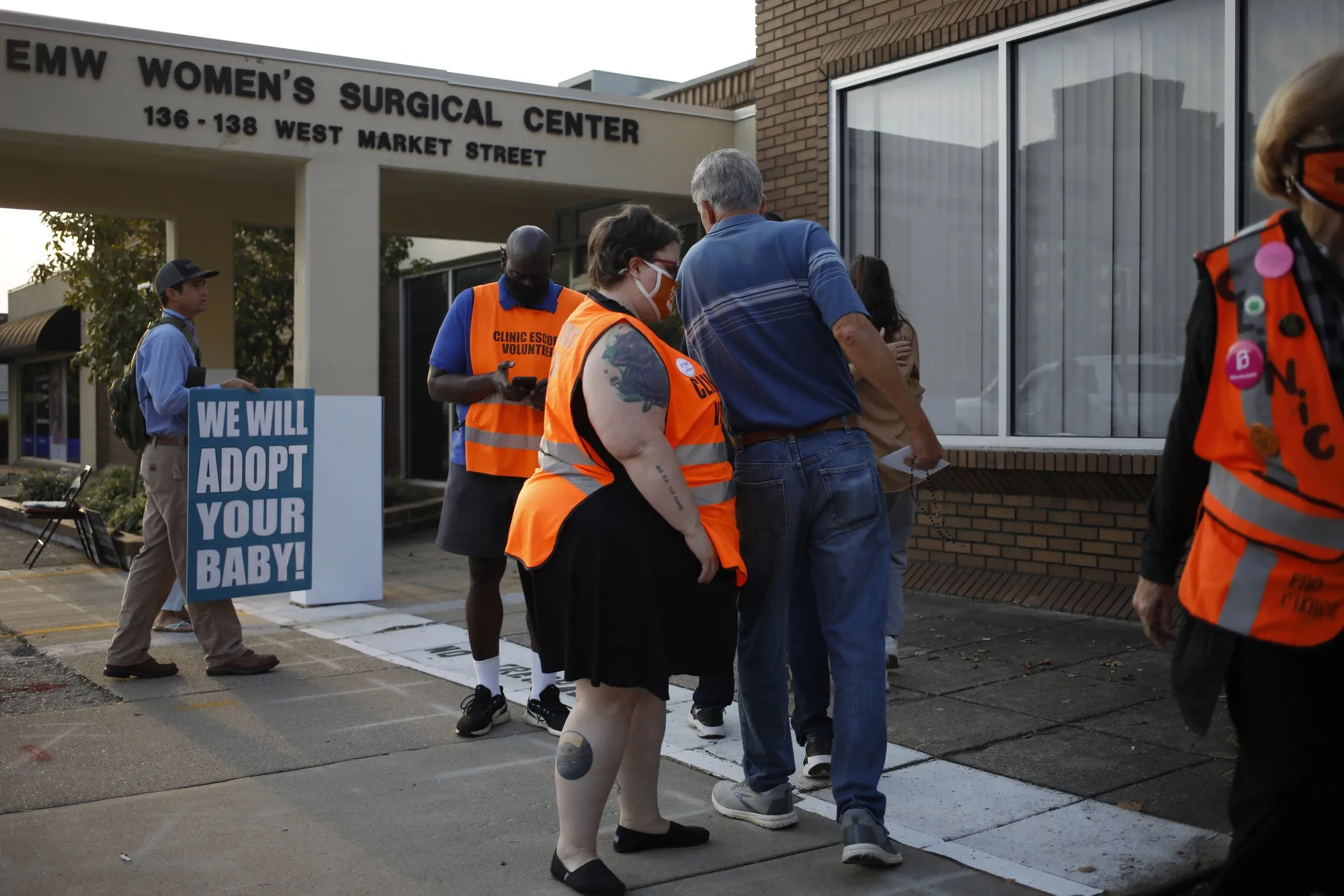 Volunteer clinic escorts wait near demonstrators outside the EMW Women's Surgical Center in Louisville, Kentucky, U.S., on Tuesday, Sept. 28, 2021.