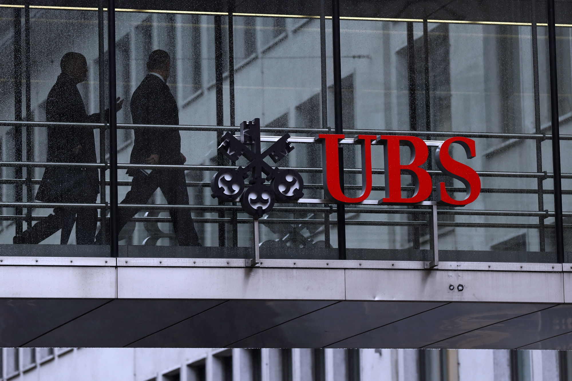 Employees pass between offices as UBS Group AG logo sits on a walkway at the UBS headquarters in Zurich, Switzerland, on Monday, Jan. 22, 2018. A UBS loan backed by shares of Steinhoff International Holdings NV was to blame for the majority of the Swiss bank’s 79 million francs ($82 million) in credit losses in the fourth quarter, a person with knowledge of the matter said.