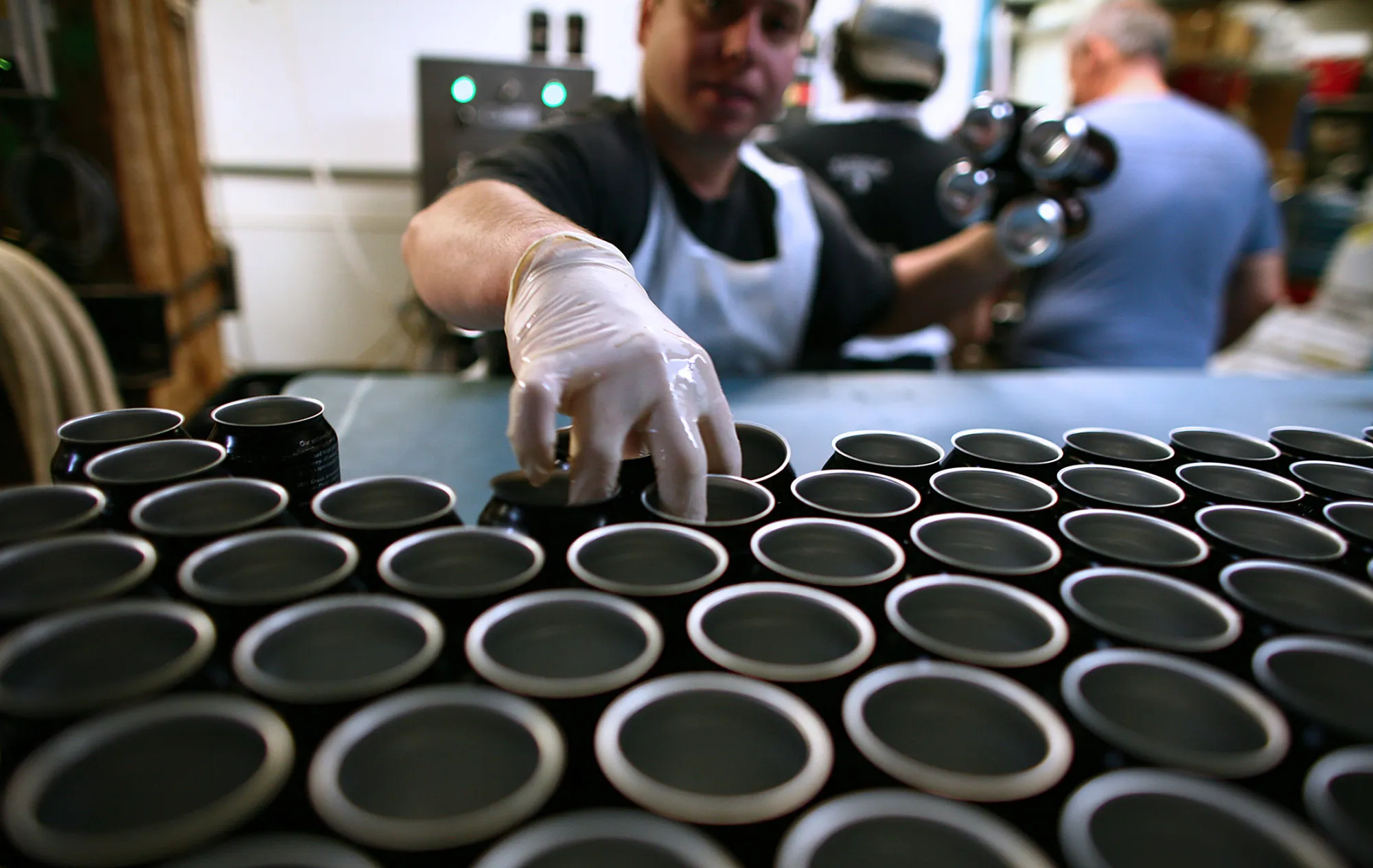 Employee Michael Knez grabs empty cans to be filled with Wynkoop Brewing Co.'s B3K Black Lager at the company's facility in Denver, Colorado, U.S., on Thursday, Jan. 26, 2012. The Wynkoop Brewing Co. was founded in 1988 by a group of entrepreneurs led by Denver's mayor John Hickenlooper.
