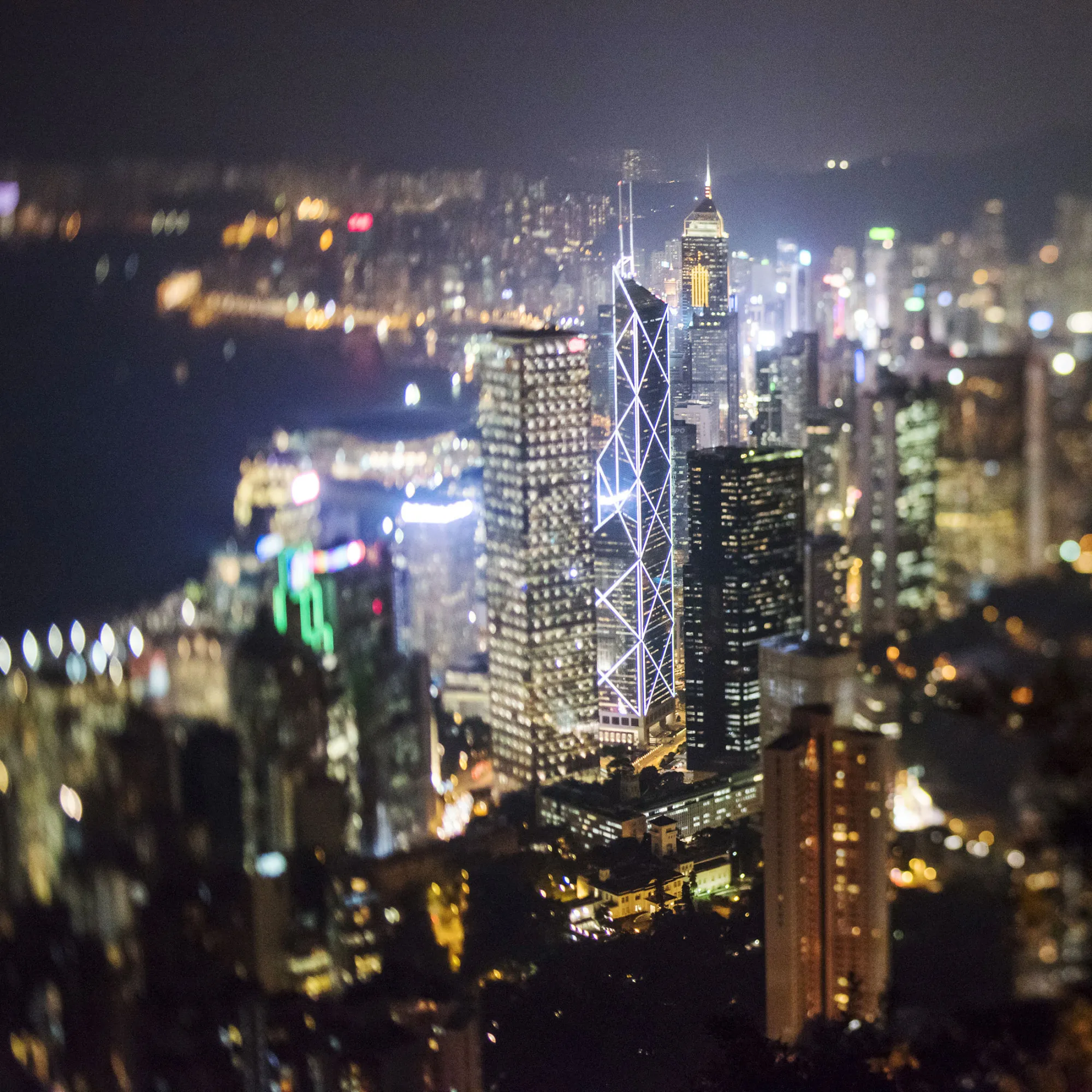 The Bank of China Tower, center left, and other commercial buildings stand illuminated at night in this photograph taken with a tilt-shift lens at night in Hong Kong, China on Friday, Nov. 27, 2015. Secondary private residential property prices dropped 3.9 percent since peaking in September, according to an index published by broker Centaline Property Agency Ltd.
