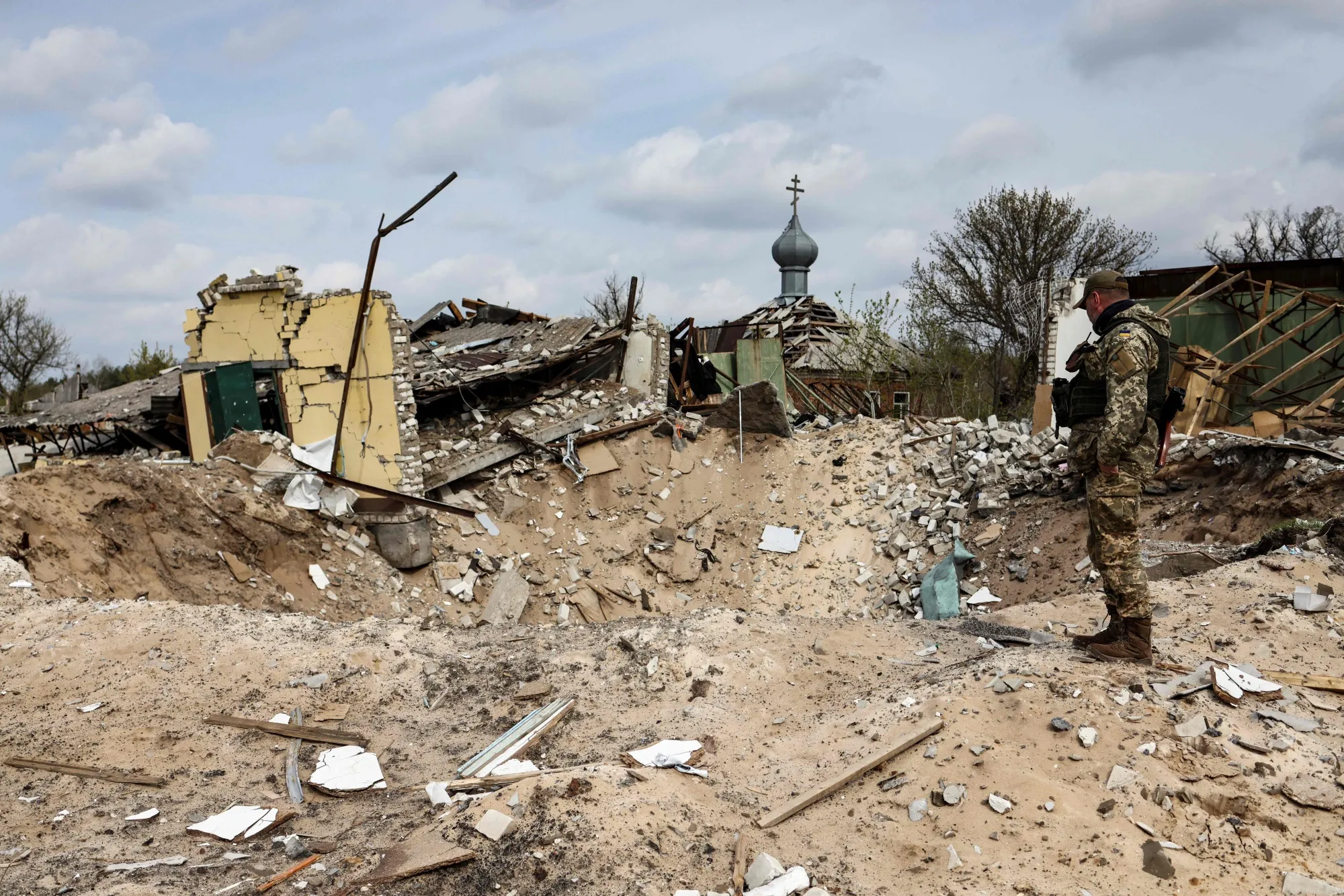 A Ukranian serviceman looks into a crater and a destroyed home in the village of Yatskivka, eastern Ukraine on April 16.
