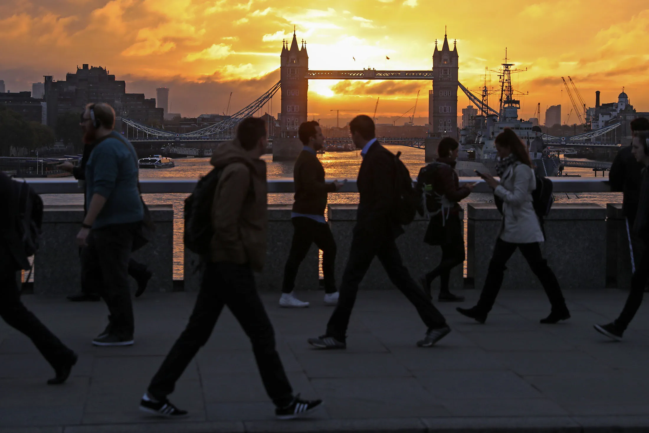 Commuters walk across London Bridge against a backdrop of Tower Bridge during sunrise in London, U.K., on Friday, Oct. 21, 2016.