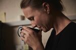 A woman holding a fresh brewed cup of coffee to her nose.